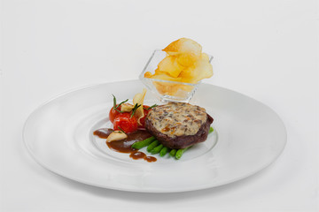 Bivstax with asparagus, tomatoes, spicy sauce on a white plate. Separately served potato chips.