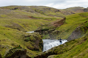 Fototapeta na wymiar Flußlandschaft in Island, Frau steht mit ausgebreiteten Armen vor Wasserfall und genießt die Faszination Natur
