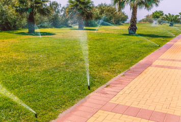 irrigation sprays watering a grass and palm tree public area along a promenade, Isla Canela, Ayamonte, Spain,