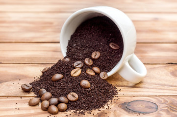 Coffee beans and ground coffee scattered from cup on the wooden background.