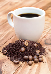 Cup of coffee with heap of ground coffee and beans on wooden table.