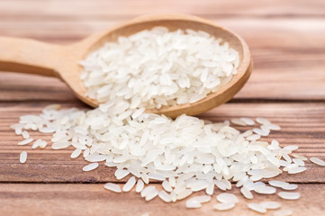 Wooden spoon with rice and pile of rice on wooden background. Close up.
