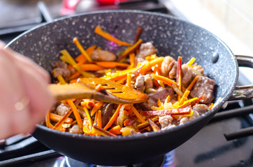 Meat with vegetables in frying pan wok on stove