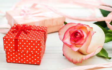 Pink rose with gift boxes on white wooden table. Close up.