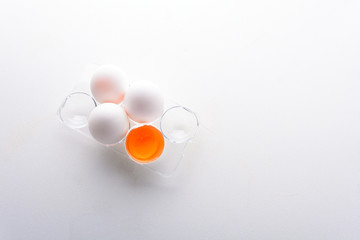 Broken egg with whole eggs in a transparent plastic container on white wooden background