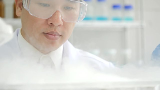 Close-up of a Medical research scientist takes out petri dish with frozen samples of cells from a cryogenic nitrogen container in a science research lab. He works in a busy modern laboratory center.