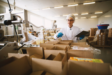 Young female worker in sterile clothes is using tablet to check right number of packages.