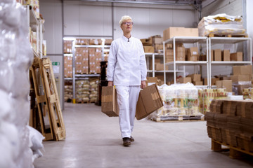 Tired female worker carrying cardboard in storage room.