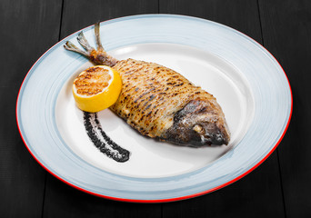 Grilled dorado fish with lemon and truffle sauce on plate on wooden background. Delicious dish of...