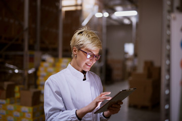Young female manager is using tablet in storage room of a factory.