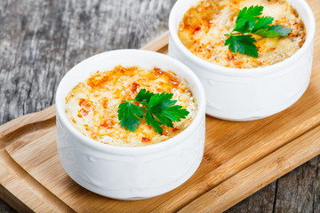 Two bowls of hot Julienne with juicy chicken, mushrooms, cream sauce and cheese on cutting board on wooden background