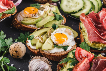 Various of sandwiches and bruschetta with prosciutto, fried quail egg, avocado, cucumber, tomatoes, spices and greens