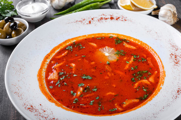Soup with meat, olives, herbs and lemon in plate, served with sour cream, peppers on dark wooden background. Homemade food