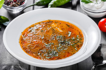 Soup chicken - broth with noodles, herbs, pepper and vegetables on plate on dark wooden background. Homemade food