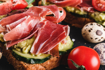 Various of sandwiches and bruschetta with prosciutto, fried quail egg, avocado, cucumber, tomatoes, spices and greens