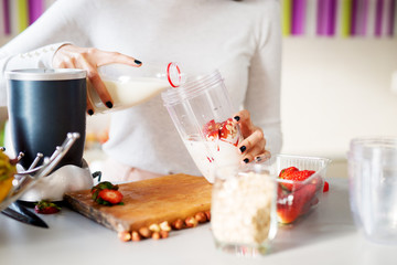 Mixer bowl is being filled with milk and fruits for a smoothie.