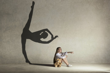 Baby girl dreaming about dancing ballet. Childhood and dream concept. Conceptual image with shadow of ballerina on the studio wall