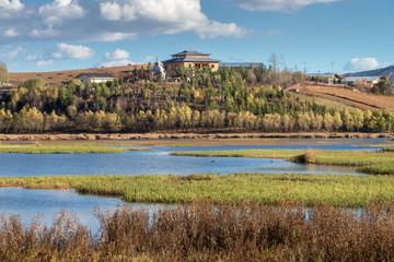 Small Buddhism pavilion surrounded by.trees near the Songzanlin Monastery lake in dry greenery field in clear blue sky day, Shangri-la, Zhongdian, Yunnan, China