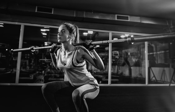 Close up of a young strong fitness female model doing squats with weight.