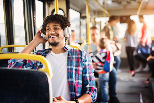 Young Afro-American man is sitting in a bus with headset on his head and listening to the music.