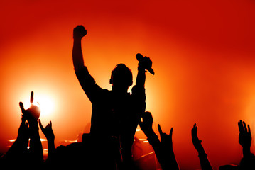 Fototapeta premium silhouette of a singer performing on stage at a concert in the fog. the vocalist raised his hand with the microphone. fans show the sign of the horn