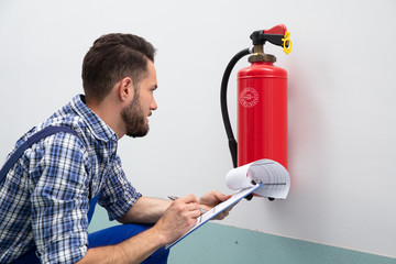Man Checking Fire Extinguisher Writing On Document
