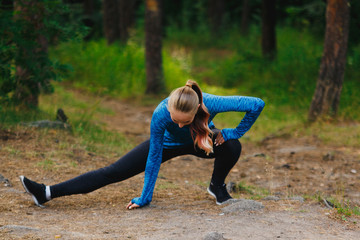 Girl in blue sportswear doing exercises outdoors in coniferous forest. Legs stretching in deep side lunge.. Healthy lifestyle sport concept.
