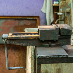 Old metal manual vise tool, in the home workshop on workbench. Vice is tool for industrial works. Selective focus. For instagram format. Square.