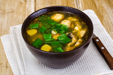 Vegetable broth with champignons and spring onions in brown bowl