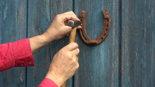 Hammering hanging old rusty horseshoe on blue wooden door with hammer