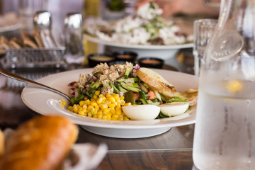 Salad with corn, melon, egg, greens, cucumber, tomato, breadcrumbs in white, among other instruments on the table