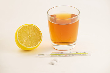 Hot tea with lemon, tablets and thermometer on white background. Healthy concept. Glass mercury thermometer with a high temperature.