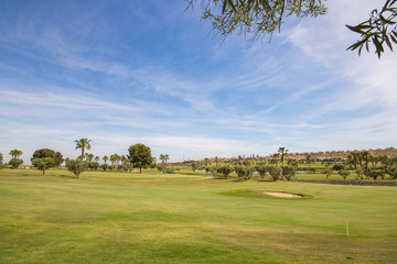 Golf course with lake, palm trees and sand pits in the Costa Blanca on a summer day with blue sky.