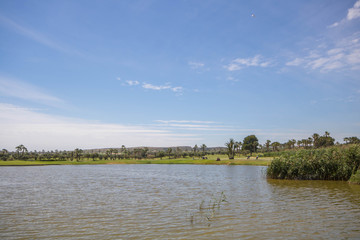 Large lake at golf course with players, buggies and trees under a blue sky on a summer day in Spain