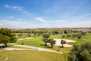 Panoramic views of golf course with sandpit, lake, trees and buggies on a summer day in Spain