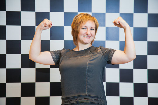 Happy woman on black and white chess geometric background. Female model show power, strong biceps jesture