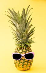 A funny image of a pineapple standing upright and wearing sunglasses on a yellow background