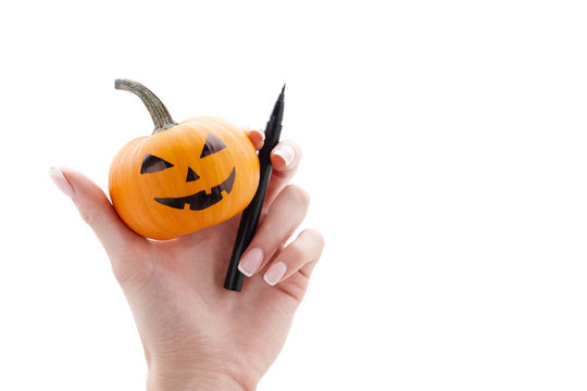Woman's hand holding small painted halloween pumpkin and black marker pen isolated on white background. Holiday decoration concept.