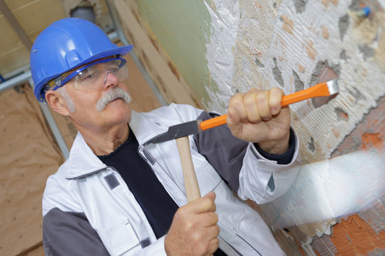 senior builder using a hammer to remove walls plaster