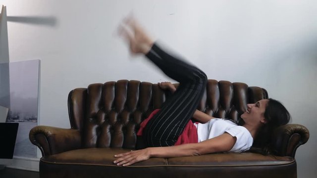 Young Woman Lying on Couch Giddily Kicking Legs in the Air