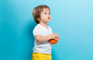 Fototapeta na wymiar Toddler boy holding a pumpkin for halloween on a blue background