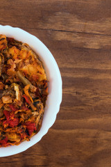 White bowl with vegetable stew cut in half on wooden background, top view, vertical frame.