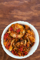 Appetizer of fried zucchini, cut into rings, with onions, carrots and tomatoes, in a white porcelain bowl on a wooden background, top view, vertical frame.