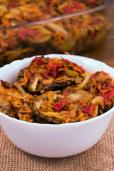 Zucchini, cut into circles and fried with tomatoes, onions, carrots and sweet peppers, stacked in a white porcelain bowl, close-up, vertical frame.