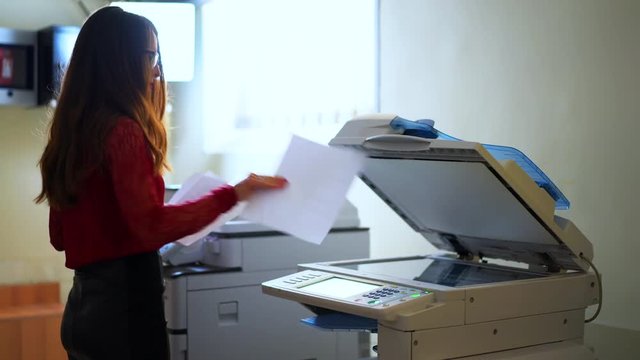 Brunette businesswoman using laser printer for making copies of documents. Professional female in office working with financial photocopies and papers. Shot in 4K (UHD).