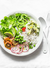 Coconut rice and vegetables buddha bowl. Vegetarian healthy lunch - rice, salad, avocado, radish, tomatoes on a light background, top view