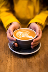 Female hands holding a latte on a wooden table.