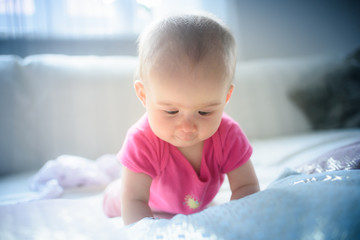 Fototapeta premium Sweet adorable baby girl lying on a couch looking towards camera. 6-7 months old infant on belly lifting upper body