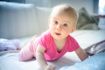 Sweet adorable baby girl lying on a couch looking towards camera. 6-7 months old infant on belly lifting upper body