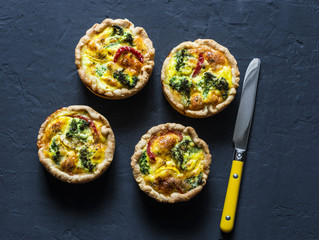 Broccoli cheddar mini savory pies on dark background, top view. Delicious appetizers, snack, tapas. Copy space